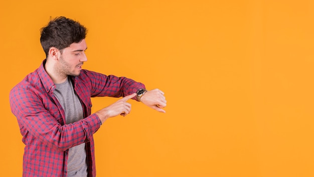 Hombre joven que controla el tiempo en su reloj de pulsera contra el fondo naranja