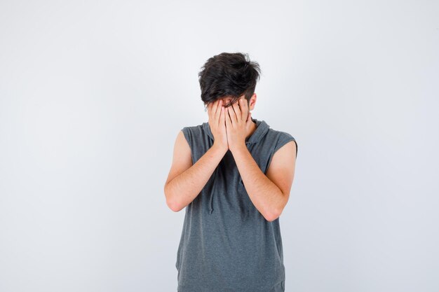 Hombre joven que cubre la cara con las manos en camiseta gris y parece serio