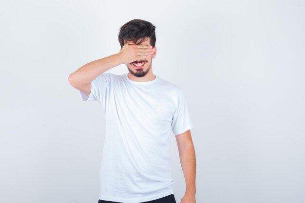 Hombre joven que cubre los ojos con la mano en la camiseta y se ve lindo