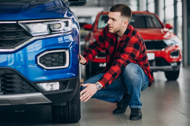 Hombre joven que elige un coche en una sala de exposición de automóviles