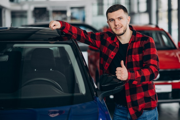 Hombre joven que elige un coche en una sala de exposición de automóviles