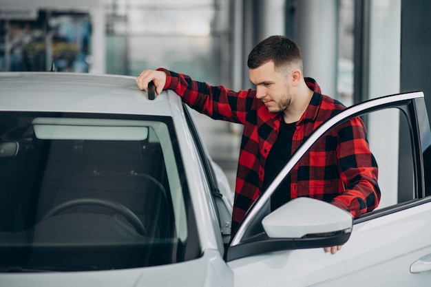 Hombre joven que elige un coche en una sala de exposición de automóviles