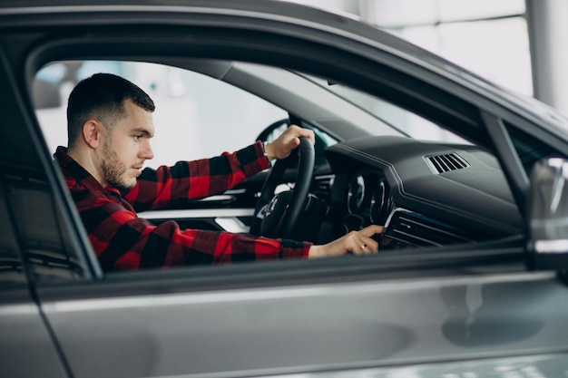 Foto gratuita hombre joven que elige un coche en una sala de exposición de automóviles