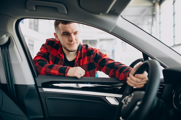 Hombre joven que elige un coche en una sala de exposición de automóviles