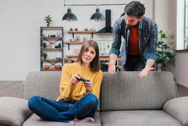 Hombre joven que grita a su esposa que juega el videojuego en casa