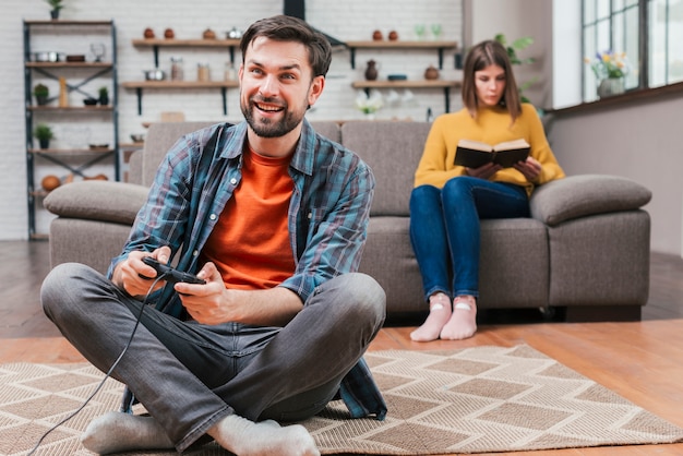 Hombre joven que juega el videojuego con la palanca de mando y su esposa que se sientan en el sofá en el contexto