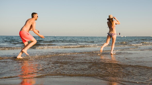 Hombre joven que lanza el chapoteo del agua sobre su novia cerca del mar en la playa