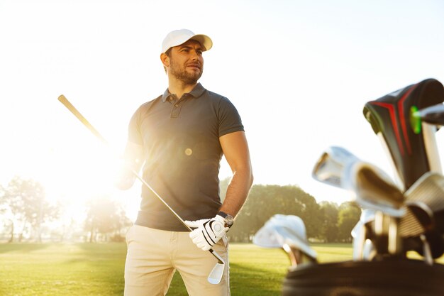 Hombre joven que lleva el club de golf mientras está de pie en el campo