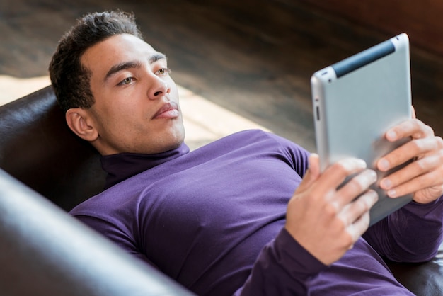 Foto gratuita hombre joven que miente en el sofá que mira la tableta digital