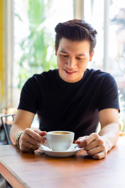 Hombre joven que mira el café caliente en la taza blanca