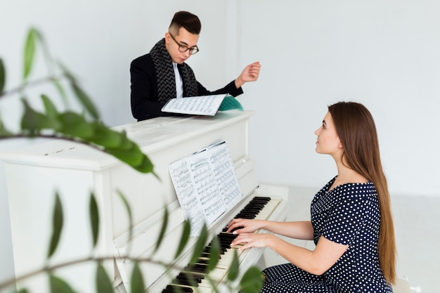 Hombre joven que mira la hoja musical que ayuda a la mujer que toca el piano