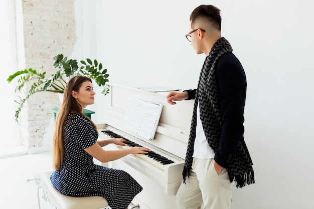 Hombre joven que mira a la mujer hermosa que toca el piano