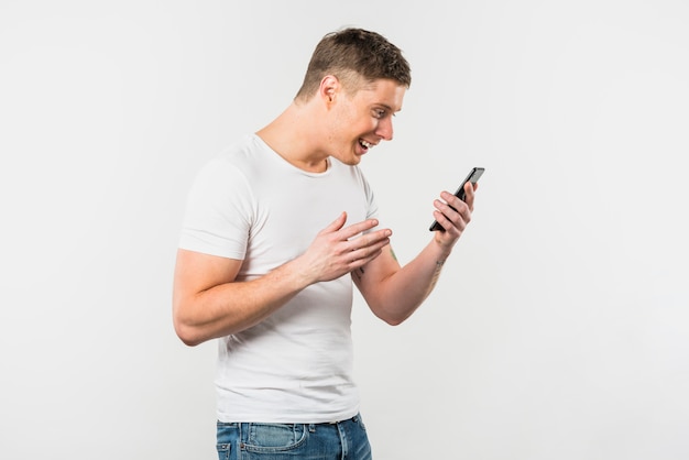 Hombre joven que mira el smartphone que sonríe contra el contexto blanco