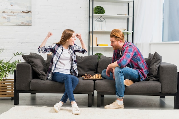 Hombre joven que mira a su novia que anima con éxito mientras que juega al ajedrez