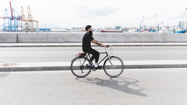 Hombre joven que monta la bicicleta en el camino cerca del puerto