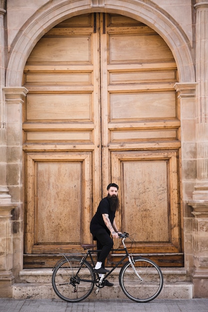 Hombre joven que monta la bicicleta delante de gran puerta cerrada