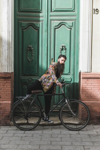 Hombre joven que monta la bicicleta delante de gran puerta cerrada