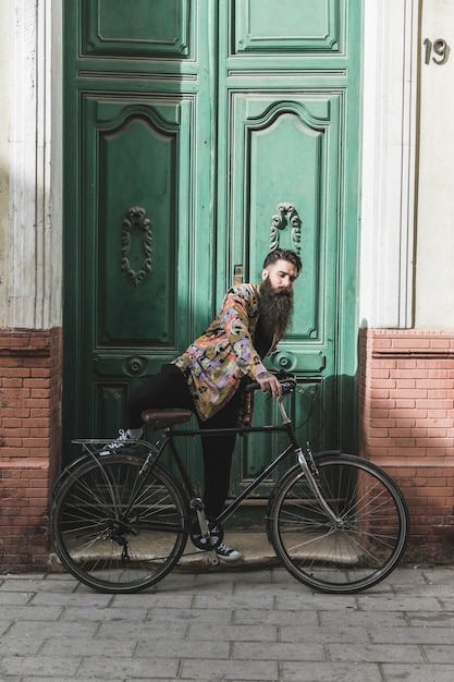 Hombre joven que monta la bicicleta delante de gran puerta cerrada