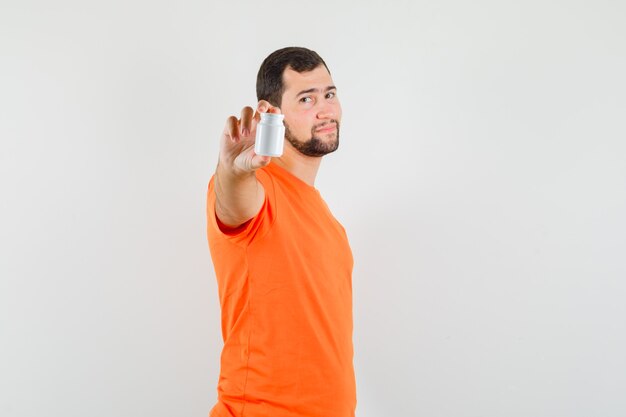 Hombre joven que muestra la botella de píldoras en camiseta naranja y parece seguro.