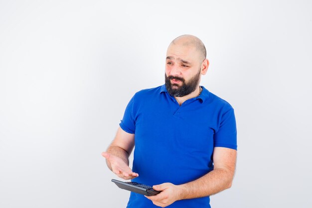 Hombre joven que muestra la calculadora mientras habla con camisa azul y mira enfocado. vista frontal.