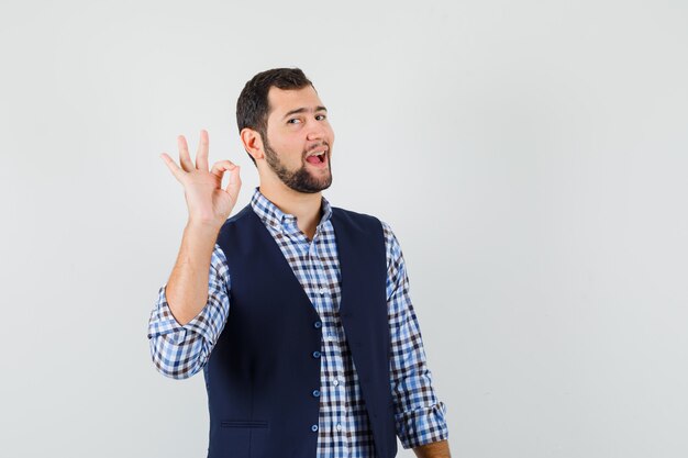 Hombre joven que muestra un gesto aceptable en camisa, chaleco y parece seguro.