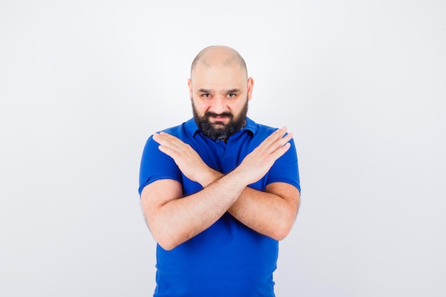 Hombre joven que muestra gesto cerrado en camisa azul y parece reacio. vista frontal.