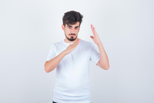 Hombre joven que muestra el gesto de chuleta de karate en camiseta y parece seguro