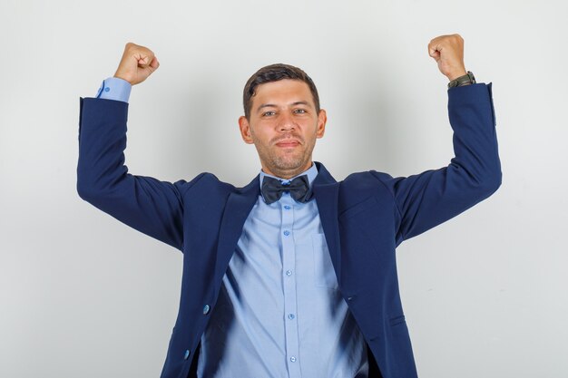 Hombre joven que muestra el gesto del ganador en traje y parece feliz.