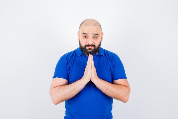 Hombre joven que muestra el gesto de namaste en la vista frontal de la camisa azul.