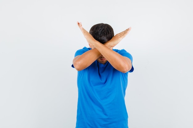 Hombre joven que muestra el gesto de la parada en la camiseta azul y parece agotado.