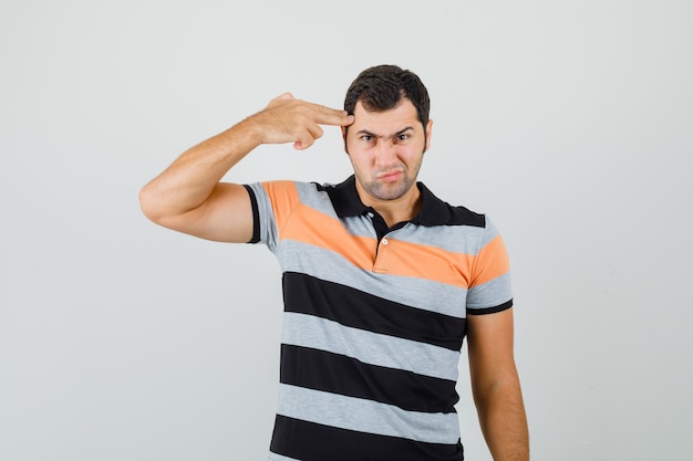 Hombre joven que muestra un gesto de pistola en la cabeza en camiseta y parece aburrido, vista frontal. espacio para texto