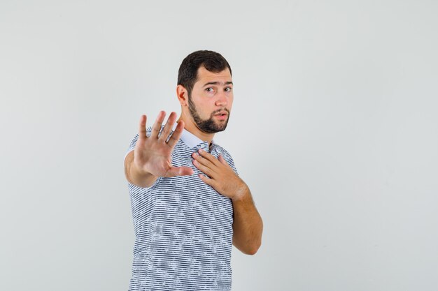 Hombre joven que muestra un gesto de rechazo apuntándose a sí mismo en camiseta y mirando serio, vista frontal.