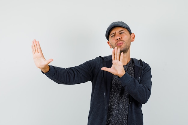 Foto gratuita hombre joven que muestra gesto de rechazo para protegerse en camiseta, chaqueta, gorra