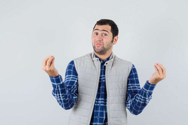 Hombre joven que muestra una opinión positiva en camisa, chaqueta sin mangas y mirando complacido, vista frontal.