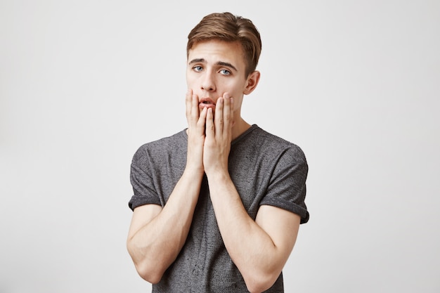 Hombre joven que parece triste y aburrido parado cerca de la pared.