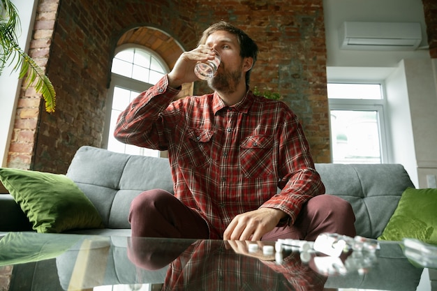 Foto gratuita hombre joven que se queda en casa, bebiendo agua y tomando pastillas