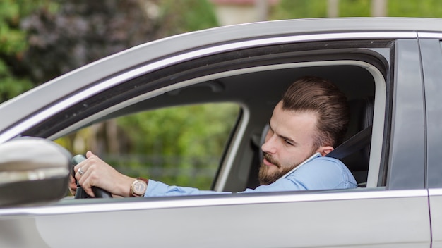 Hombre joven que se sienta dentro del coche que habla en el teléfono móvil