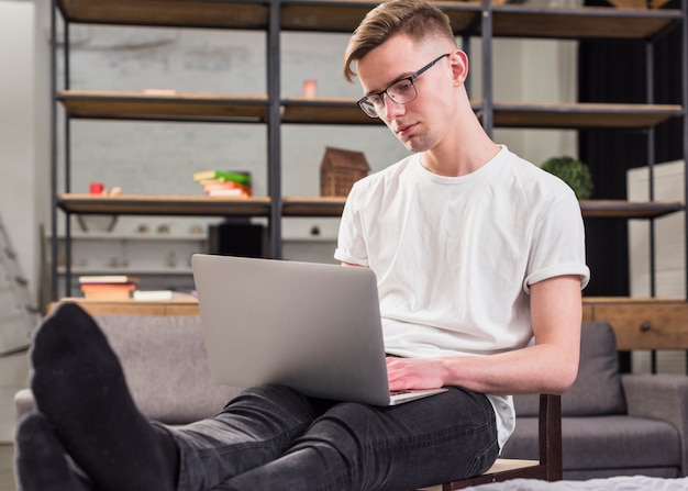 Foto gratuita hombre joven que se sienta en silla usando el ordenador portátil en casa