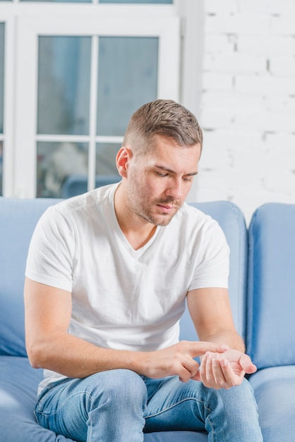 Hombre joven que se sienta en el sofá azul que comprueba su pulso