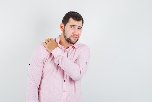 Foto gratuita hombre joven que sufre de dolor en el hombro en camisa rosa y parece cansado