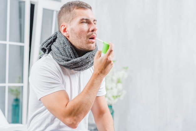 Hombre joven que sufre de frío trata su garganta con un spray