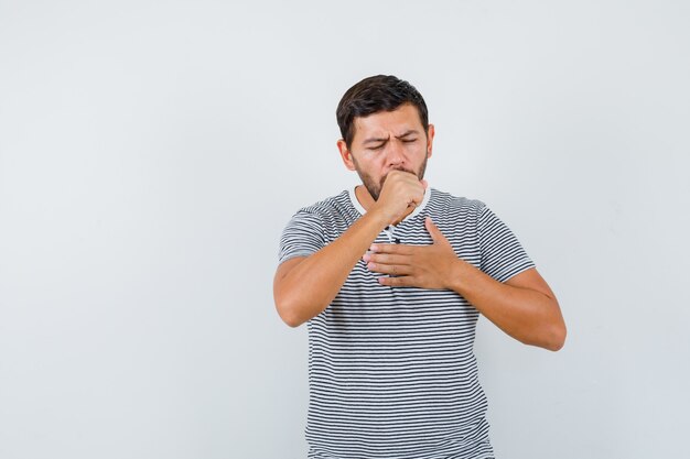 Hombre joven que sufre de tos en camiseta y parece enfermo. vista frontal.