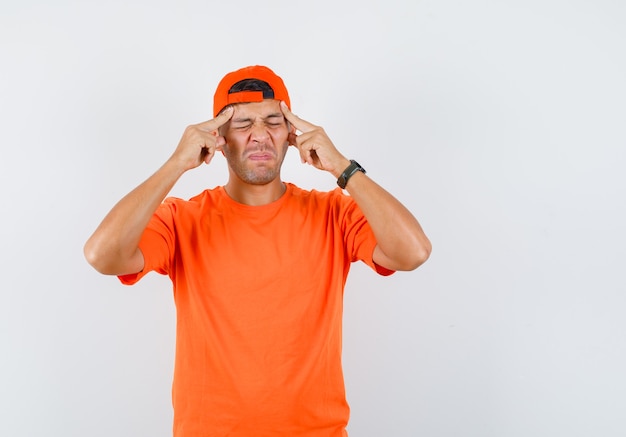 Hombre joven que tiene dolor de cabeza, masajeando las sienes en camiseta naranja y gorra