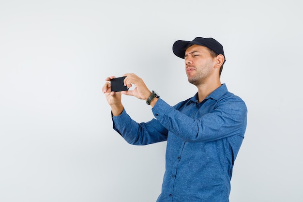 Hombre joven que toma la foto en el teléfono móvil en camisa azul, vista frontal de la tapa.