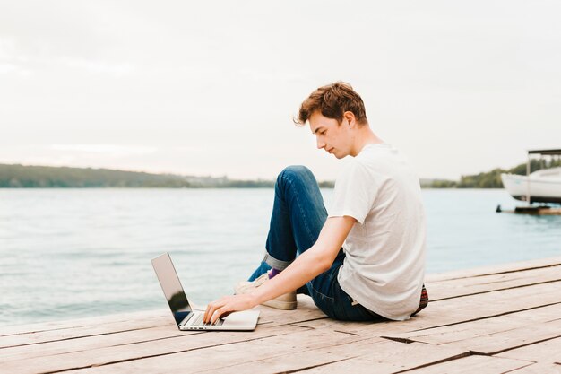 Hombre joven que trabaja en la computadora portátil por el lago