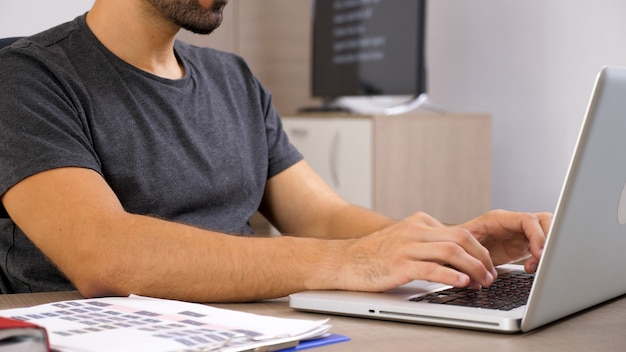 Hombre joven que trabaja con el portátil en la documentación de su empresa. Persona de negocios en el lugar de trabajo.