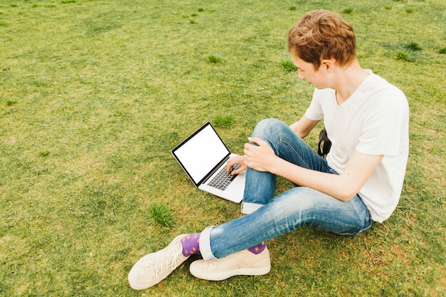 Foto gratuita hombre joven que usa la computadora portátil en hierba verde