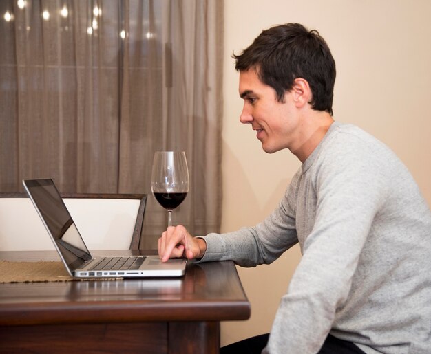 Hombre joven que usa el ordenador portátil con la copa en la tabla en casa