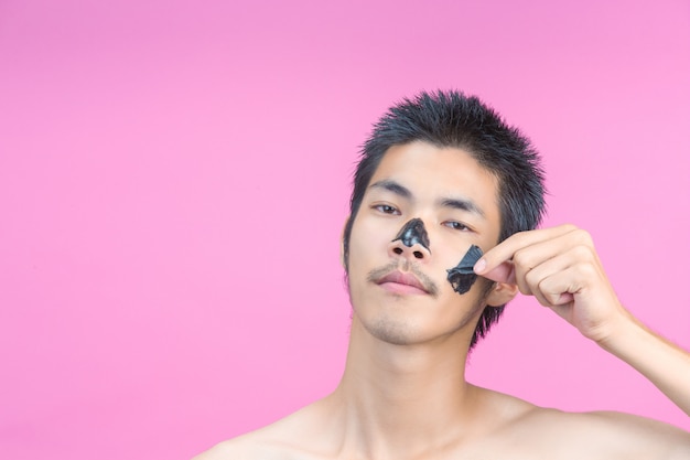 Un hombre joven que usa sus manos para quitar cosméticos negros en su rostro en un rosa.