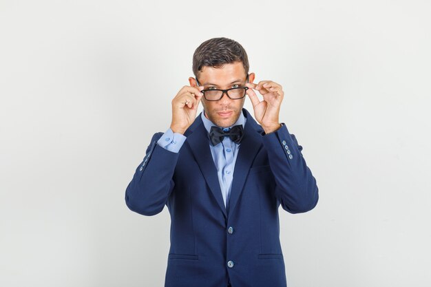 Hombre joven quitándose las gafas en traje y mirando serio.